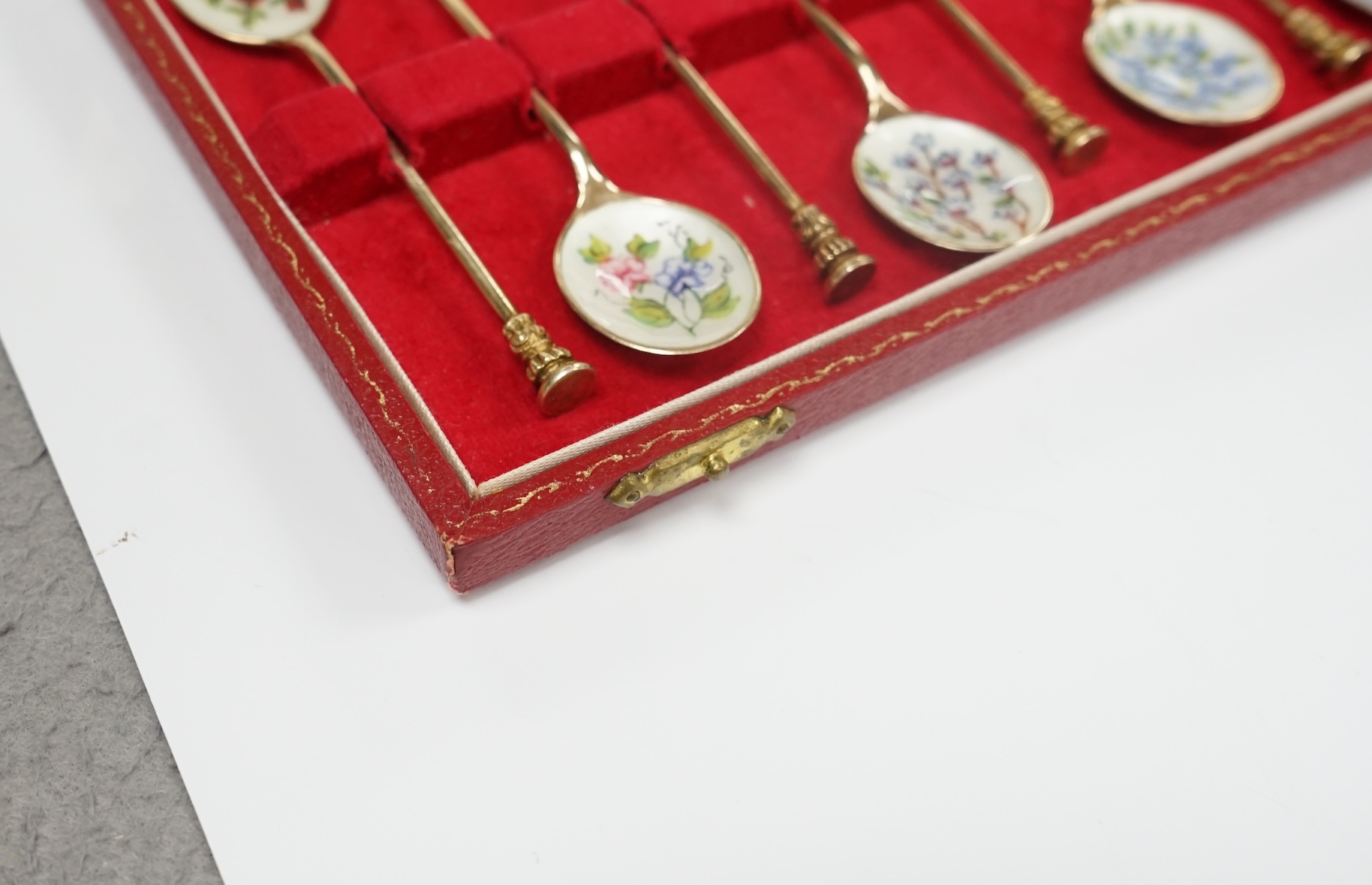 A cased set of twelve early 1970's silver gilt and enamel coffee spoons, decorated with flowers, S.J. Rose & Son, Birmingham, 1971, 98mm. Condition - fair to good